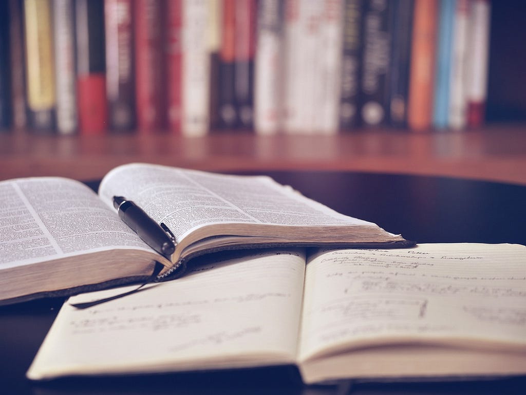 A picture of two books open in front of a library with a pen on it